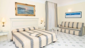 Habitación de hotel con cama, sofá, una mesita y dos cuadros en las paredes.
