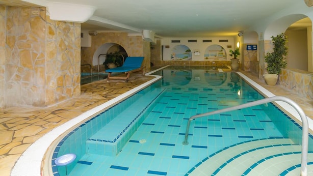 Una piscina interior con suelo de baldosas, una zona de descanso con una silla azul y paredes de piedra.
