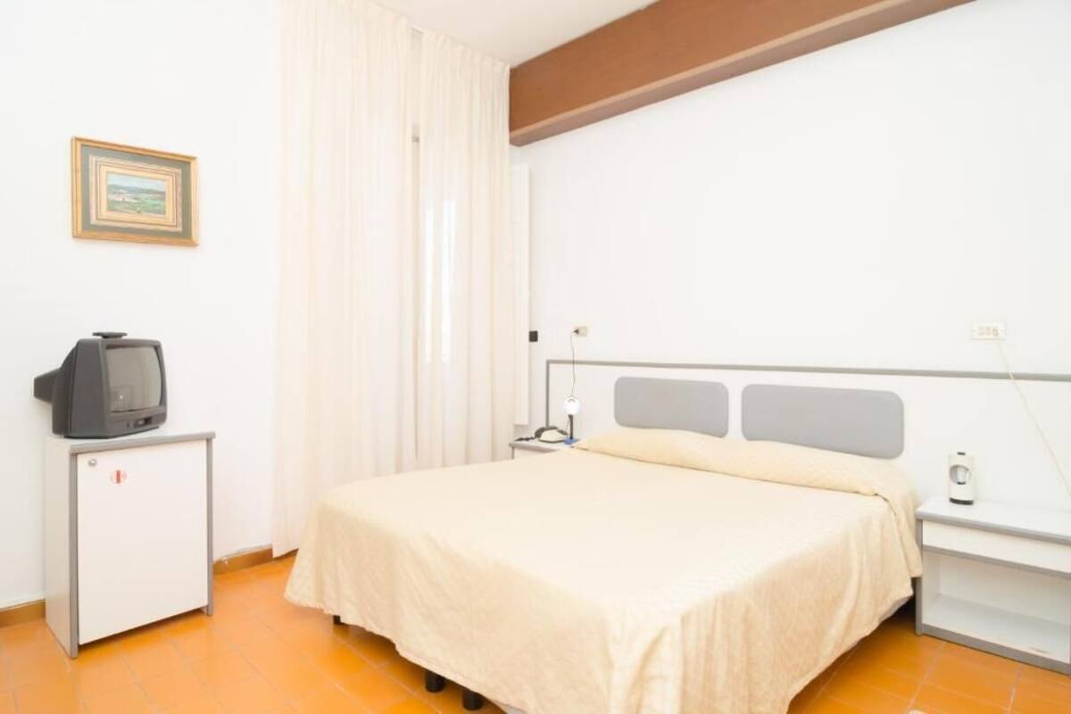A hotel room with a bed, a small TV on a cabinet, a bedside table, and a nightstand.