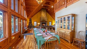 A dining room with a long table set for a meal, wooden walls, a stone fireplace, and a Christmas tree. - Spacious Cabin w/Hot Tub~2 King beds, fire pit (Slatyfork)