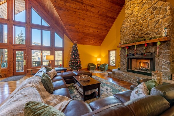 Ein gemütliches Wohnzimmer mit Kamin aus Stein, Ledersofas und einem Weihnachtsbaum.