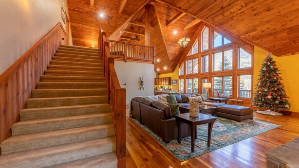 A spacious living room with a wooden staircase, a large window, and a Christmas tree. - Spacious Cabin w/Hot Tub~2 King beds, fire pit (Slatyfork)