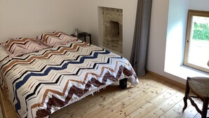 Une chambre avec un grand lit, un plancher en bois, un mur en pierre et une fenêtre donnant sur un paysage verdoyant.