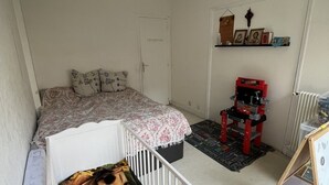 A room with a crib, a bed, a red toy car, and a shelf with pictures. - Appartement en Face de la Gare Routière de Menton (Menton)