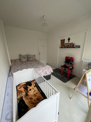 A room with a crib, a bed, a red toy car, and a shelf with pictures. - Appartement en Face de la Gare Routière de Menton (Menton)