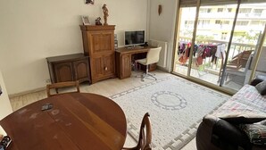 A living room with a wooden dining table, a TV, a sofa, and a view of a balcony with clothes drying. - Appartement en Face de la Gare Routière de Menton (Menton)