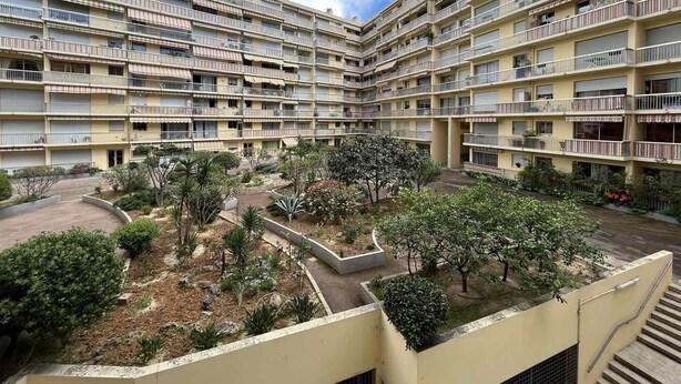 A multi-story residential building with balconies, a central courtyard with trees and shrubs, and a clear sky. - Appartement en Face de la Gare Routière de Menton (Menton)