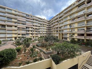 Un edificio residencial de varios pisos con balcones, un patio central con árboles y arbustos, y un cielo despejado.