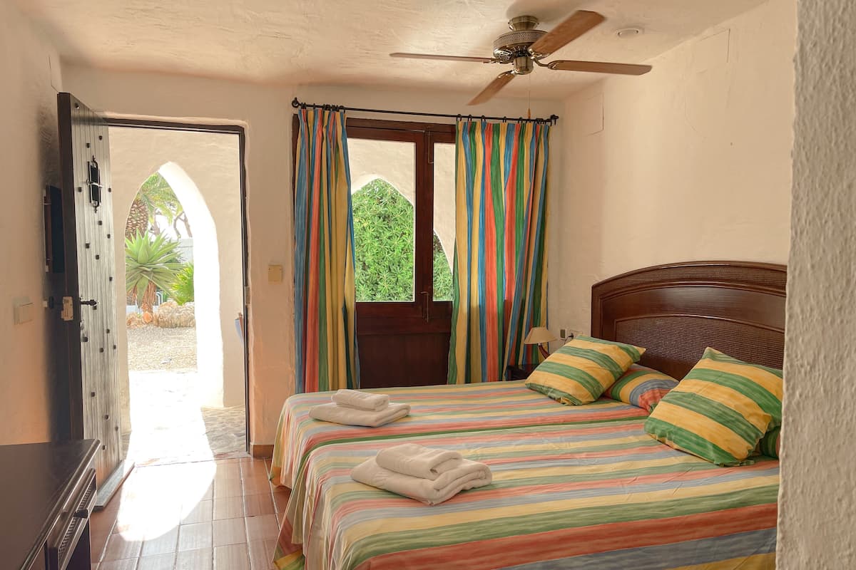 A bedroom with a bed, two pillows, a ceiling fan, and a window with curtains.