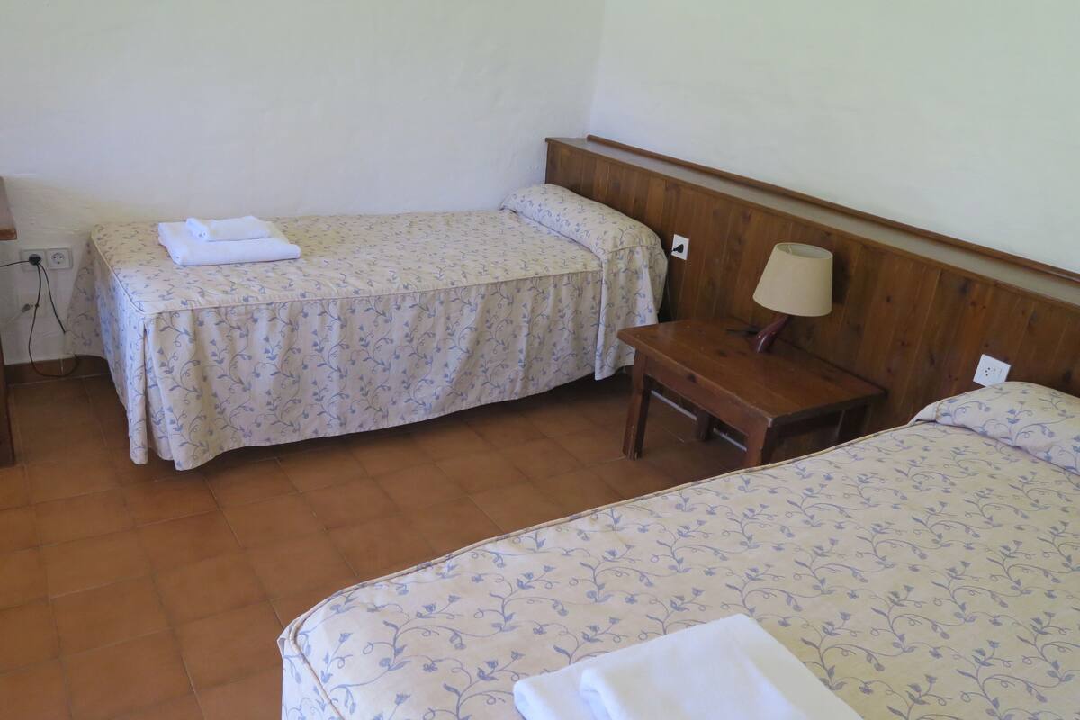 A hotel room with two beds, a wooden nightstand, a lamp, and a power outlet.