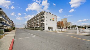 Un hotel de varios pisos con balcones, un estacionamiento y un cielo despejado.