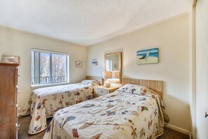 Un dormitorio con dos camas, una ventana, un espejo y un aparador.