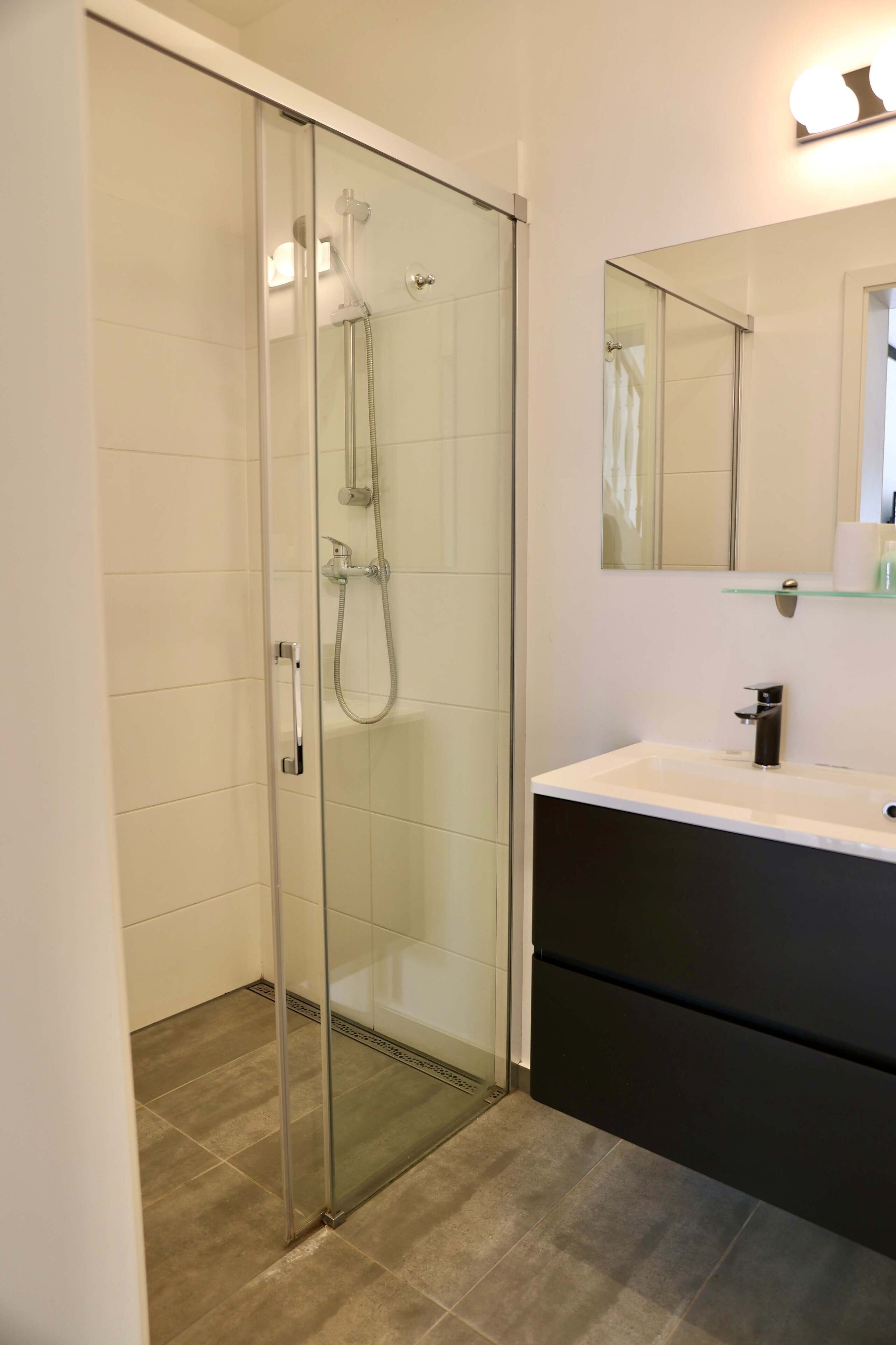 Ein modernes Badezimmer mit Duschkabine aus Glas, einem weißen Waschbecken und einem schwarzen Waschtisch.