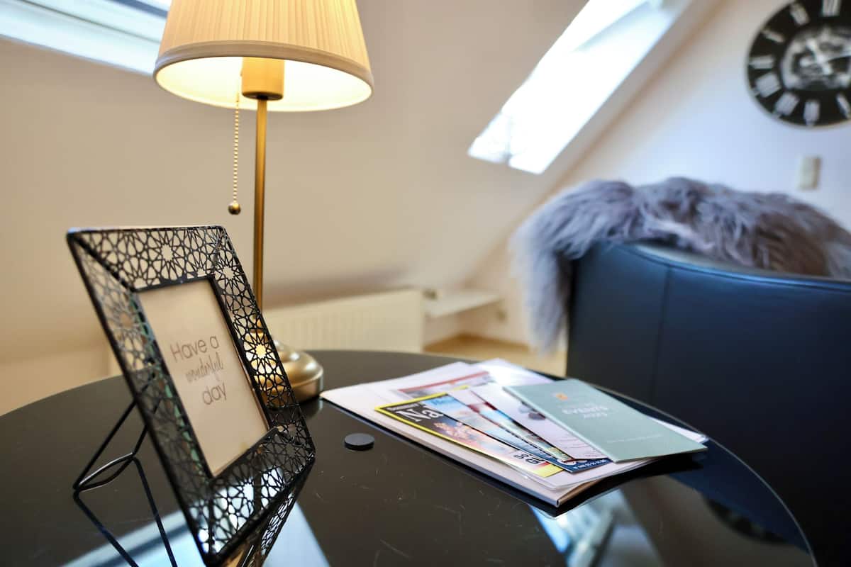 A room with a table featuring a framed picture, a lamp, and magazines.