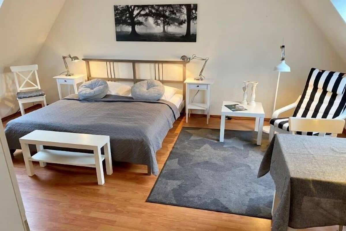 A cozy, well-lit bedroom with a large bed, bedside tables, a chair, and a desk.