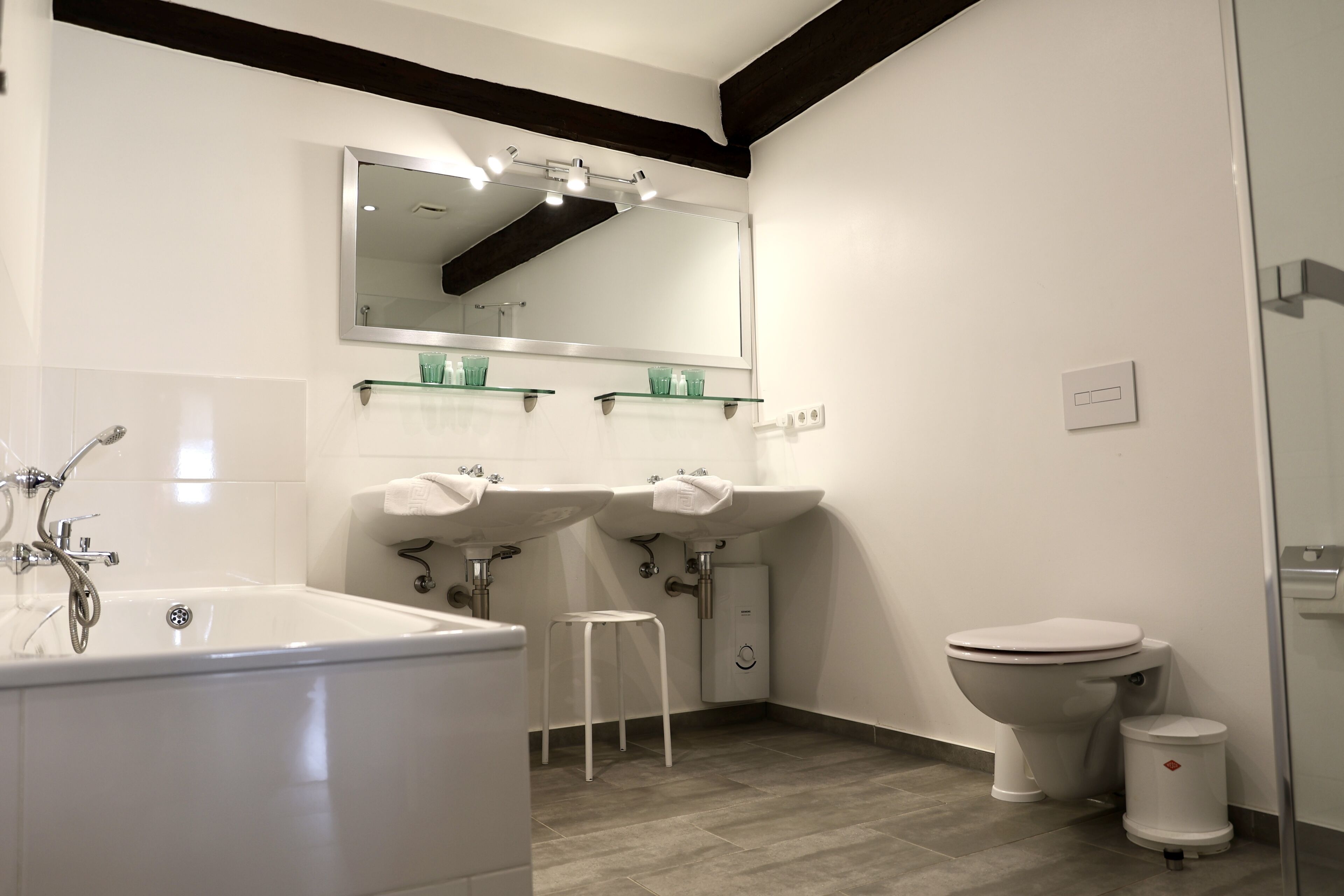 A modern bathroom with a bathtub, two sinks, a toilet, and a mirror.