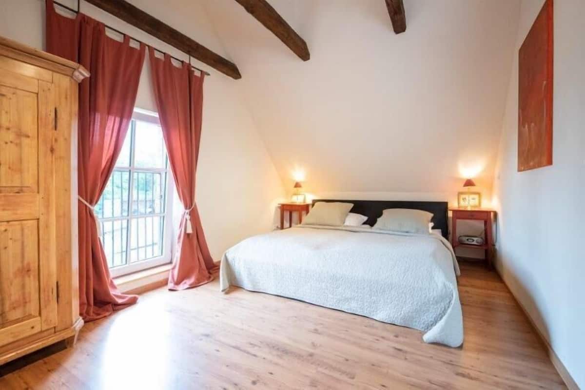 A bedroom with a large bed, wooden floor, and a window with curtains.