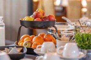 A breakfast buffet with fruits, oranges, and tea service.