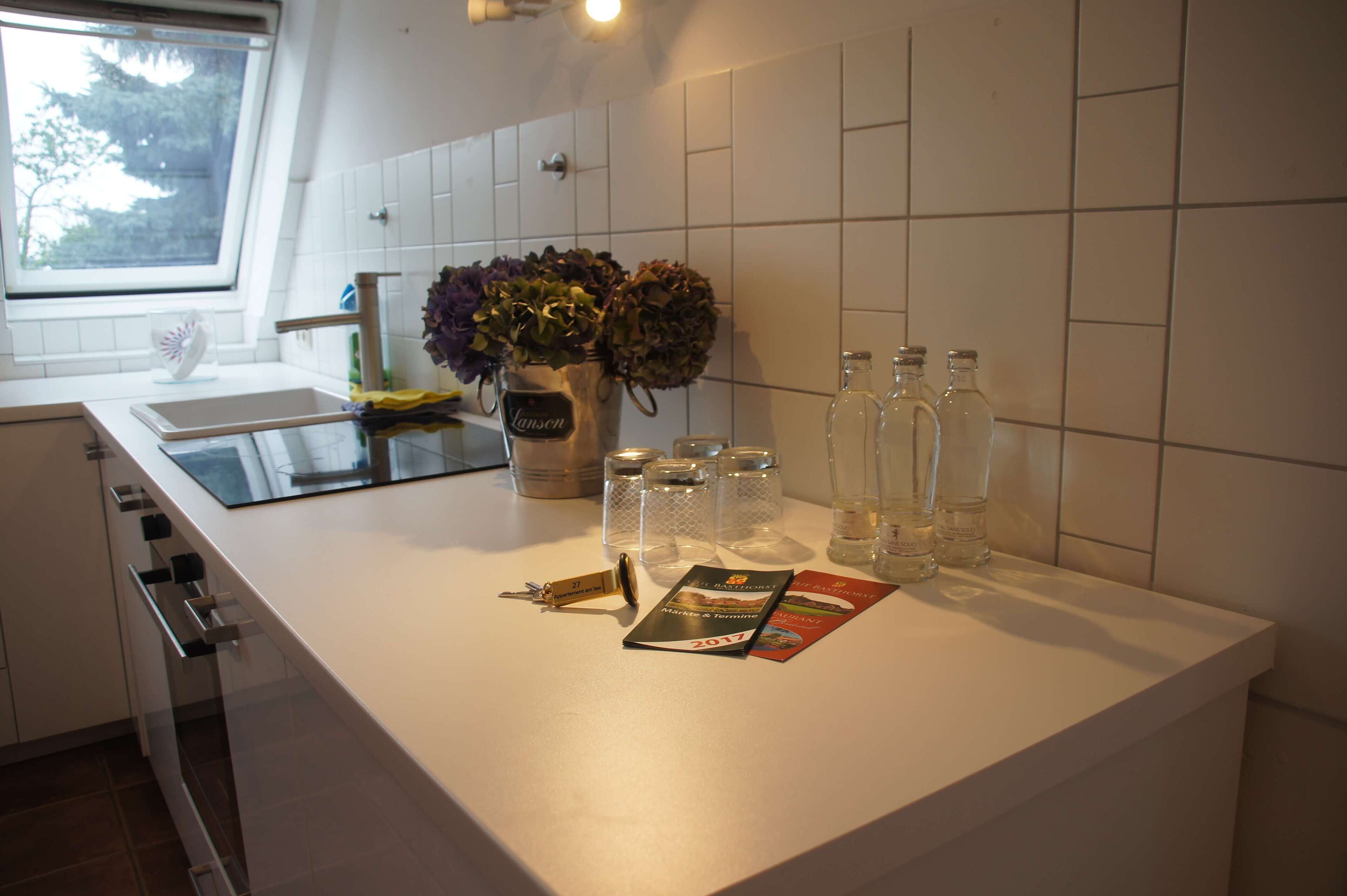A kitchen counter with a window, a vase with flowers, and several glass bottles.