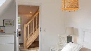Une chambre avec un escalier en bois, un lit avec une literie blanche, une table de chevet avec une lampe et un luminaire fixé au mur.