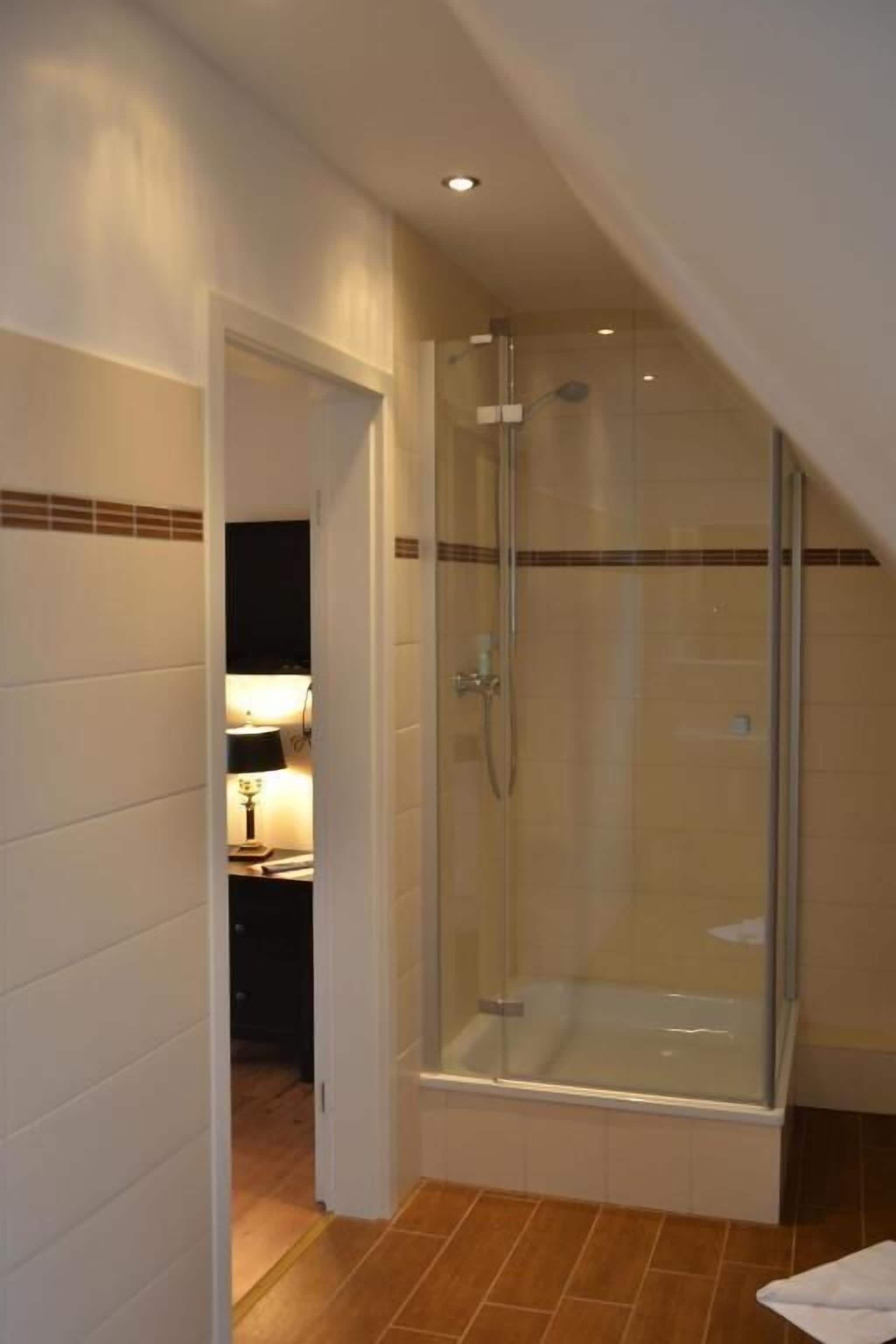 Un espace douche clos par des parois de verre, doté d’un sol carrelé, d’une serviette visible et d’une porte donnant sur une autre pièce.