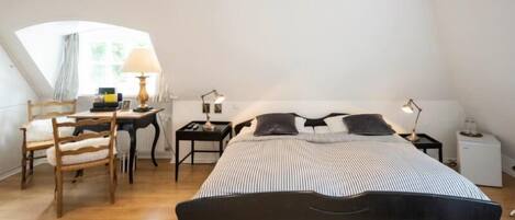 Un dormitorio con una cama, un escritorio, dos sillas y una lámpara.