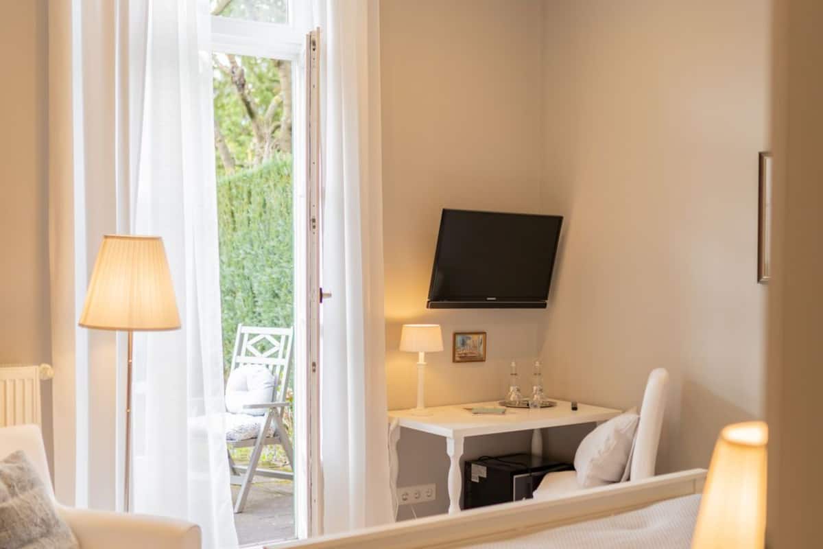 A hotel room with a bed, a desk with a TV, a chair, and a lamp.