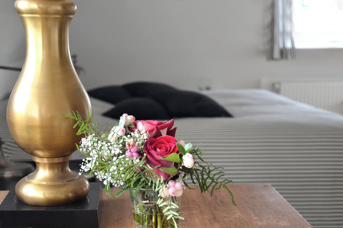 A brass vase with a bouquet of flowers on a wooden table in a hotel room.