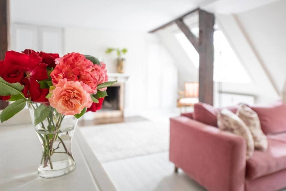A modern living room with a pink sofa and a vase of flowers on a white table.
