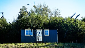 Et lille, etetagers hus med to vinduer og en dør, omgivet af frodig vegetation og træer.