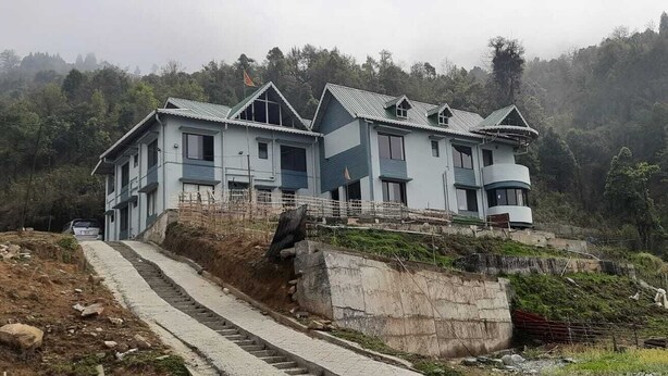Un edificio de varios pisos con una escalera pronunciada que lleva a él, rodeado por una ladera boscosa.