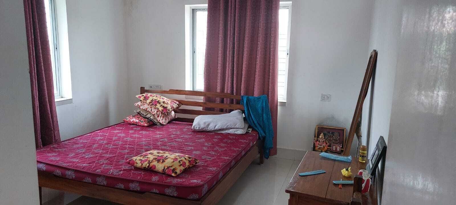A bedroom with a bed, a wooden headboard, a bedside table with a mirror, and a window with curtains.