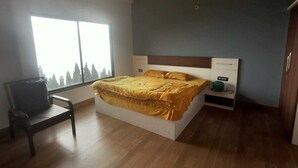 Un dormitorio con cama, una silla, una mesita de noche y ventana con vistas a árboles.