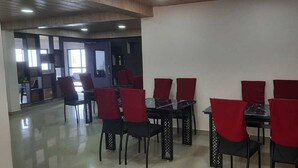Un comedor con mesas y sillas, una cocina al fondo y vistas al exterior.