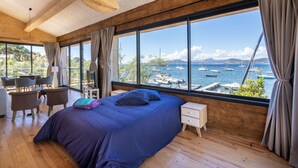 Un dormitorio con una cama grande, pisos de madera, un escritorio y vistas a barcos y montañas.