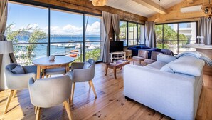 Un salón moderno con un ventanal que da a un puerto deportivo, suelo de madera y muebles contemporáneos.