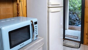 Una cocina con un microondas azul sobre una encimera de mármol, un refrigerador blanco, armarios de madera y una puerta que da a un jardín.