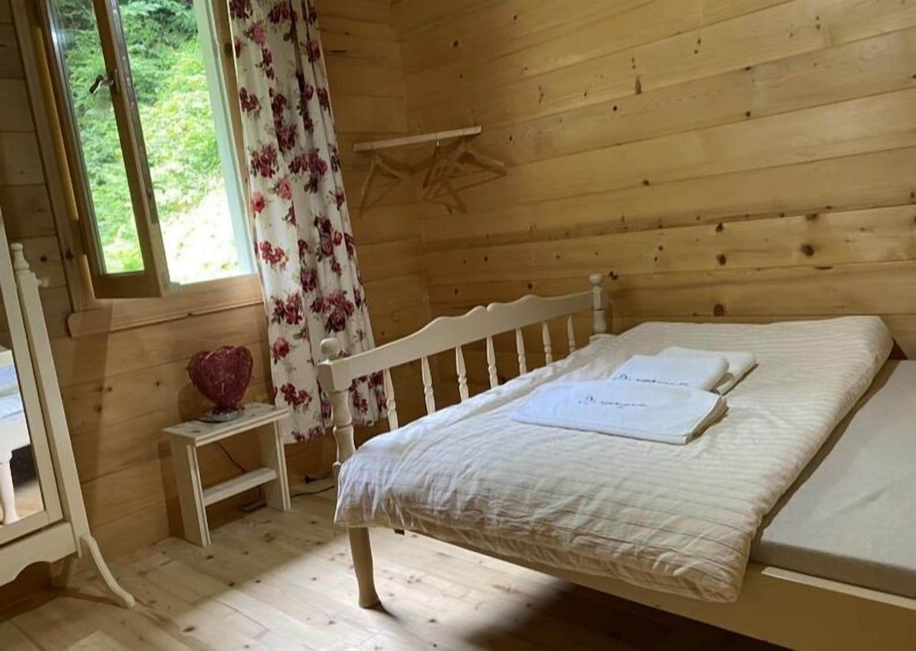 Ein Schlafzimmer einer Holzhütte mit einem Einzelbett, einem kleinen Nachttisch und einem Fenster mit floralem Vorhang.
