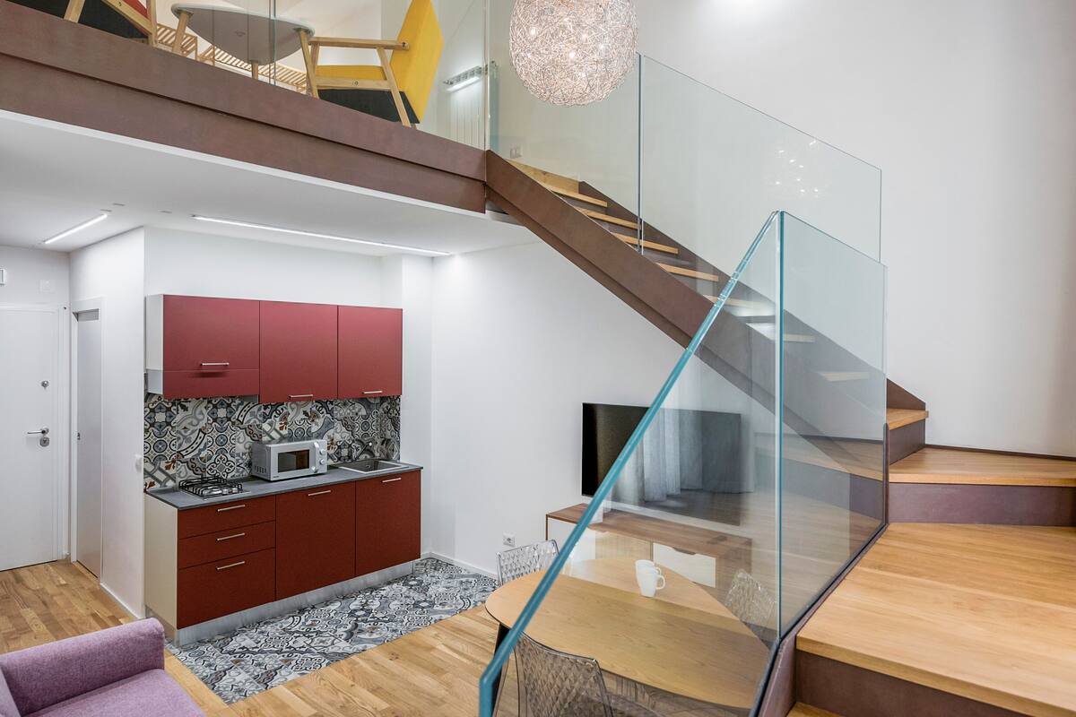A modern kitchen with red cabinets, a microwave, and a patterned backsplash.