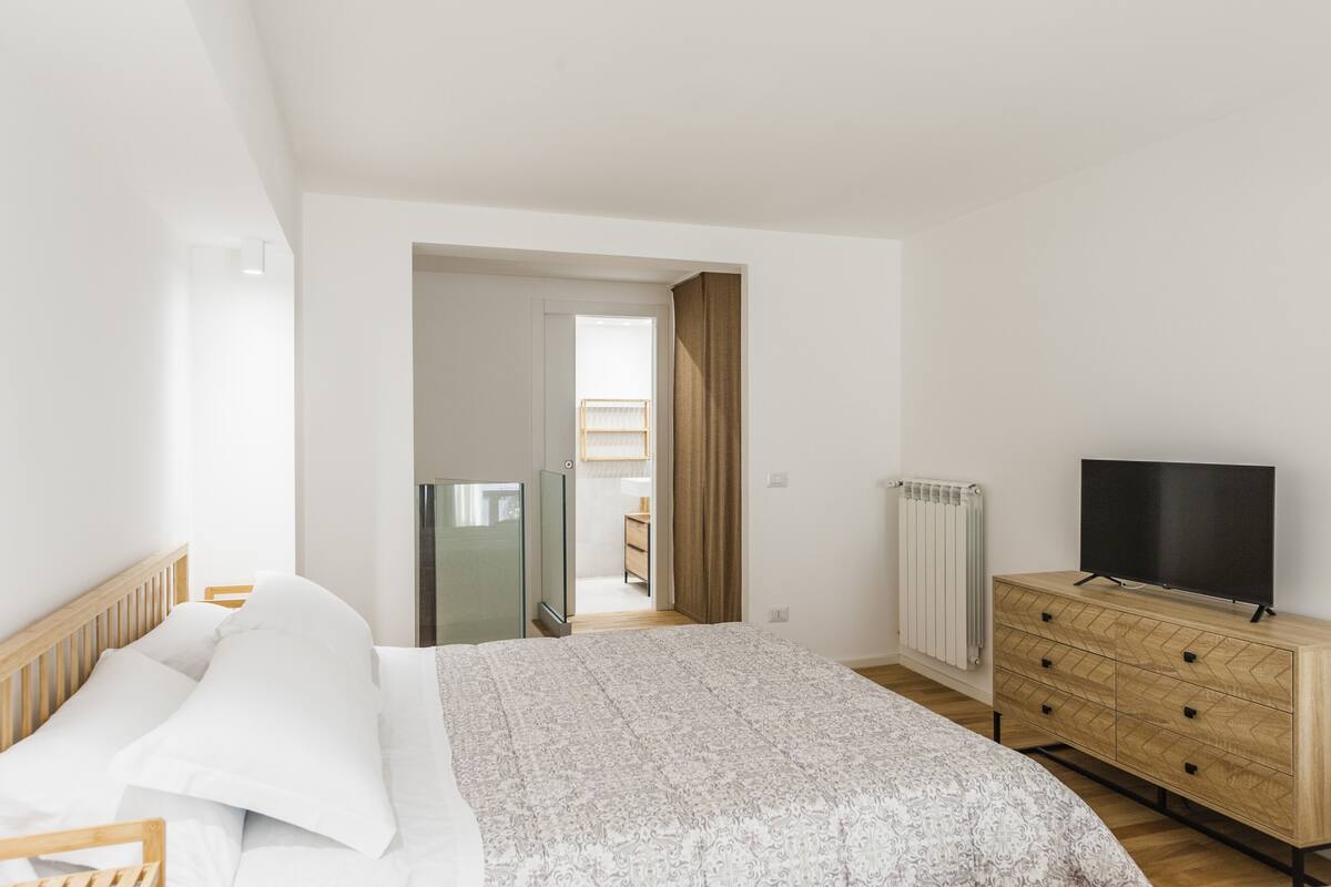 A bedroom with a bed, a dresser, a TV, and a radiator.
