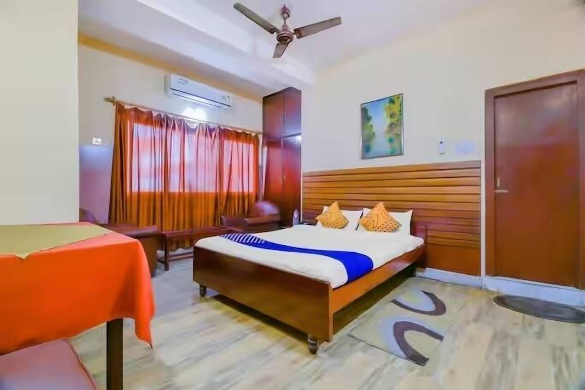 A hotel room with a bed, a table, a ceiling fan, and a door.