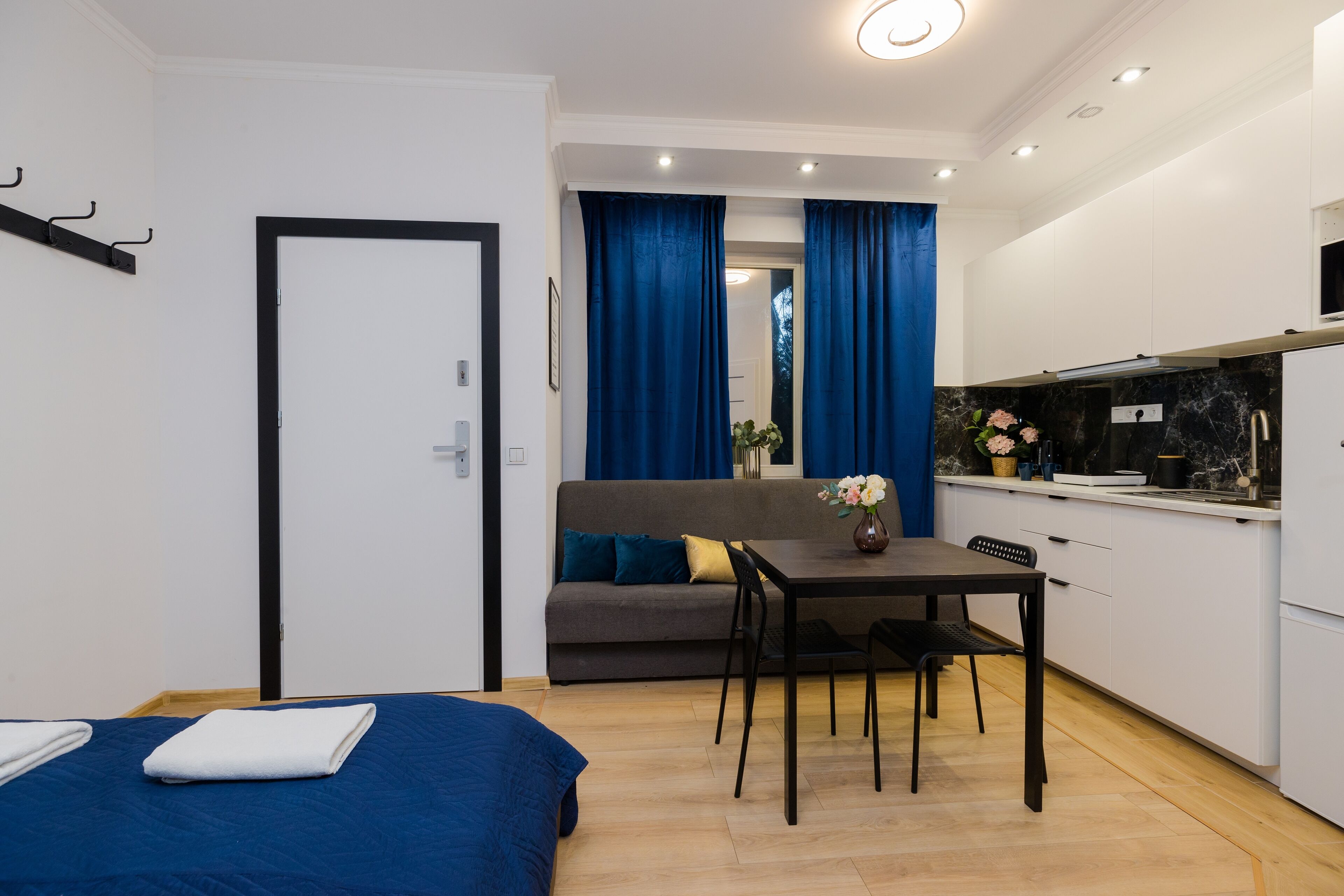 A compact room with a bed, a sofa, a dining table, and a kitchenette.