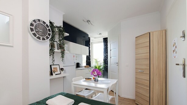 Une chambre à coucher de taille modeste, comprenant un lit, une petite table ornée d’un vase de fleurs, une horloge et une armoire.