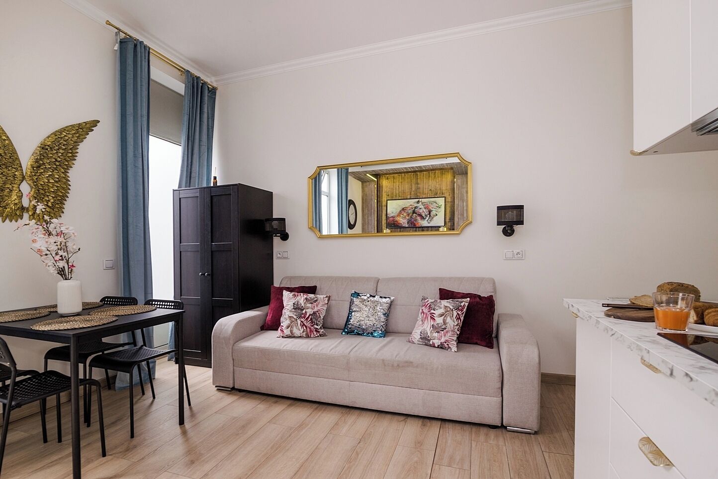 A modern living room with a sofa, a dining table with chairs, a cabinet, and a mirror.