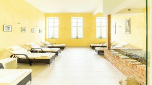Una habitación con varias tumbonas dispuestas en filas, ventanas amplias y una pared de ladrillo con una fuente de agua.
