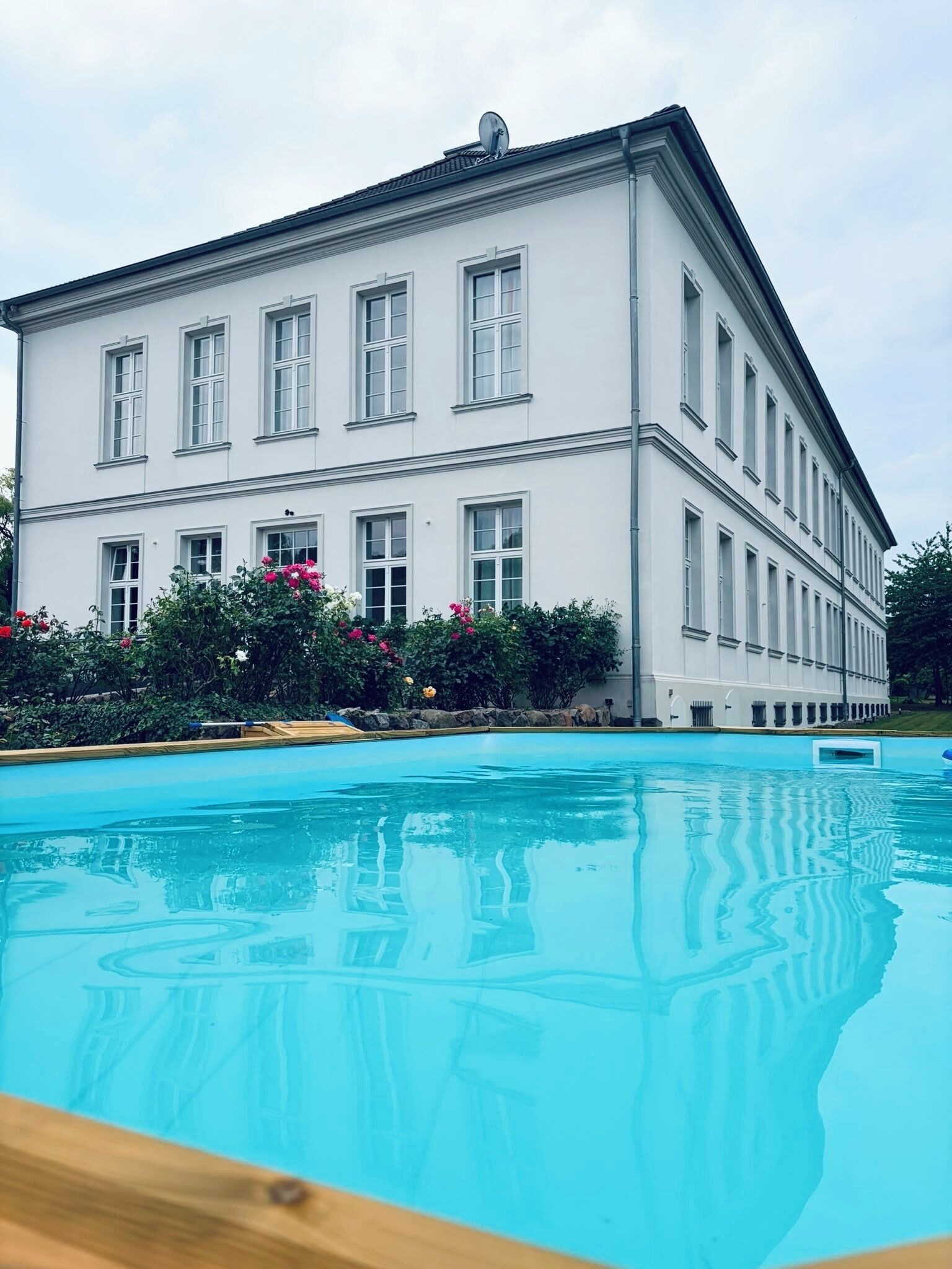 Ein großes, weißes Gebäude mit vielen Fenstern und einem Schwimmbecken davor.