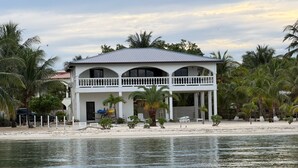 Ein Strandhaus mit Balkon, Palmen und einem Sandstrand.