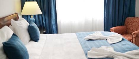 Une chambre d’hôtel avec un lit, une table de chevet avec une lampe, une chaise et une fenêtre avec des rideaux.