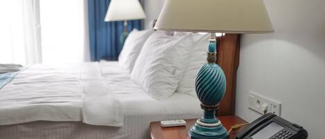 A hotel room with a neatly made bed, a bedside table with a lamp, a phone, and a remote control.