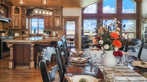A spacious kitchen with wooden cabinets, a large island, and a dining area set for six with a table set for a meal. - Spacious Cabin with Hot Tub, Fire Pit, Game Room (Island Park,)